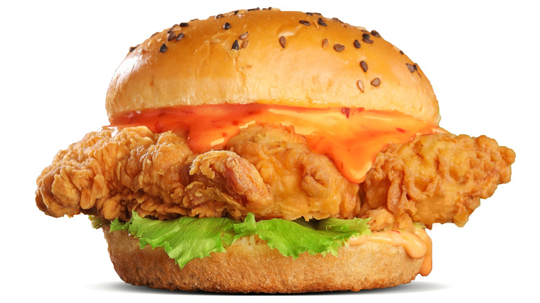 Studio shot of a delicious fried chicken sandwich with sauce on seeded bun against a white background