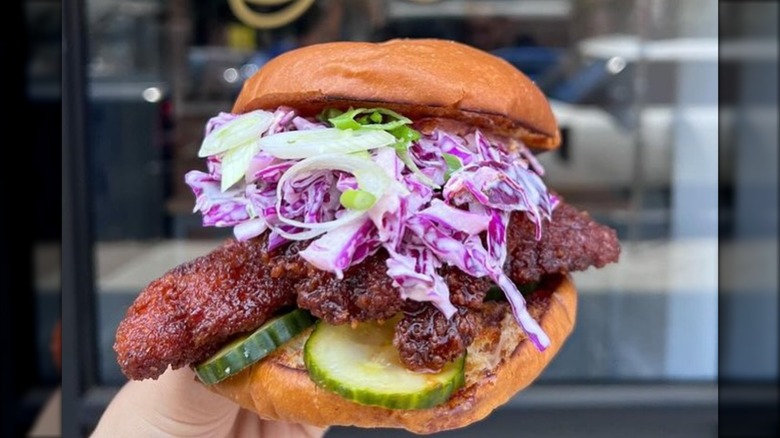 No Forks Given Korean Fried Chicken Sandwich, held in front of the restaurant's facade