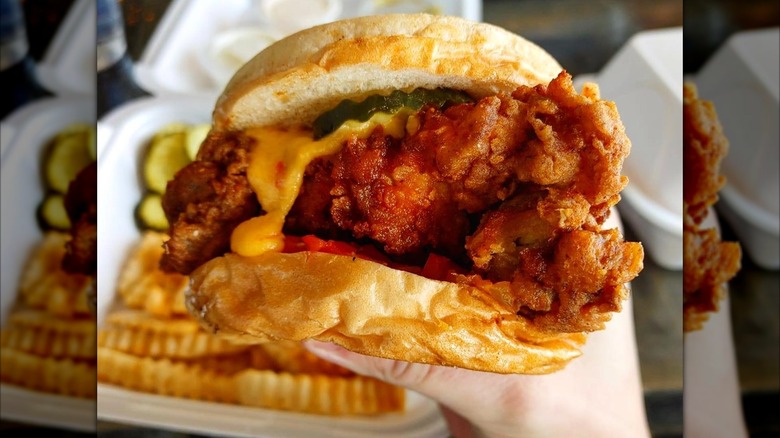 Brave Idiot Chicken Sandwich, held in close-up above the table