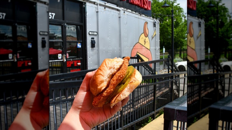 Krazy Katsu OG Chicken Sandwich held in the foreground in front of restaurant exterior