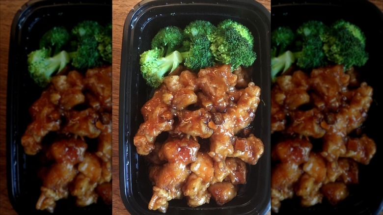 Orange chicken with side of broccoli in black to-go container.