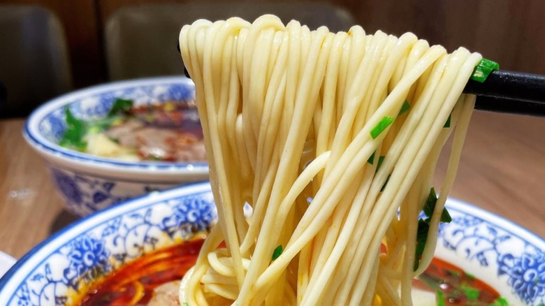 Close-up of noodles being pulled from a bowl on chopsticks from Lanzhou Hand-Pulled Noodles.