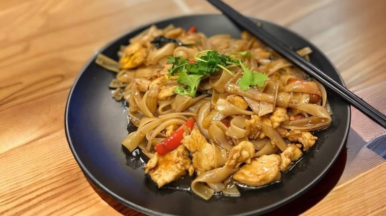 Noodle dish from Phnom Penh Restaurant, on black plate with chopsticks.