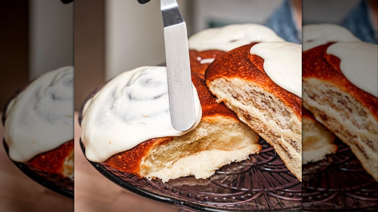 Little Loaf Bakery & Schoolhouse cinnamon rolls being iced on a cake stand with a spatula