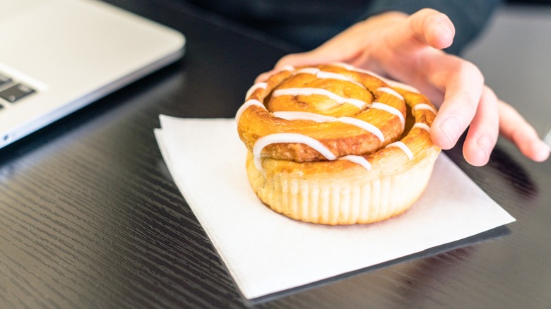 Businesswoman eating a cinnamon roll during work.