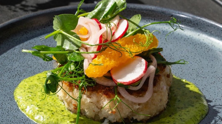 Griddled Crab Cake at Row 34 topped with radishes, onions, pea shoots, orange atop a green sauce