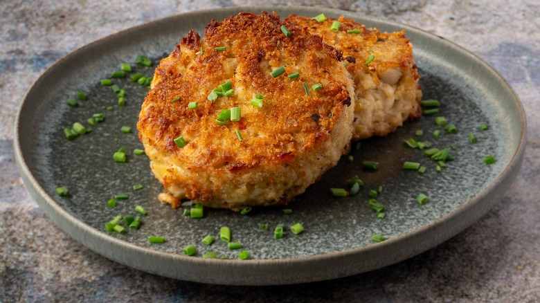 Two golden brown crab cakes on a plate garnished with chives