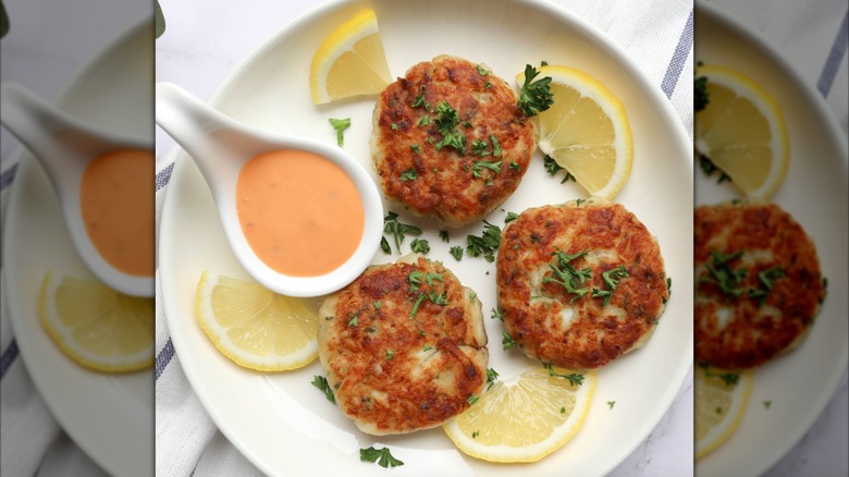 Plate of Crab Cakes with slice lemon garnish and cocktail sauce in a white spoon at Coastal Seafoods