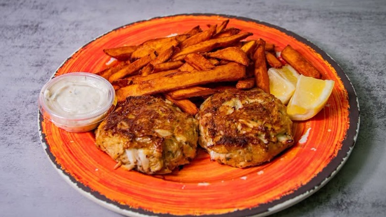 Orange plate of Crab Cakes with side of French Fries and sliced lemon garnish at Crab Corner