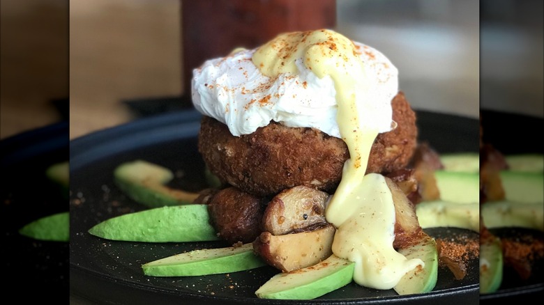 Crab Cake Benedict at Surf over country potatoes and sliced avocados on a black plate