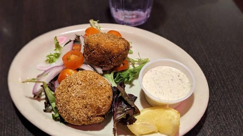 Crab cakes on salad greens with side of sliced lemon and a remoulade sauce on a white plate at Jambo Cafe