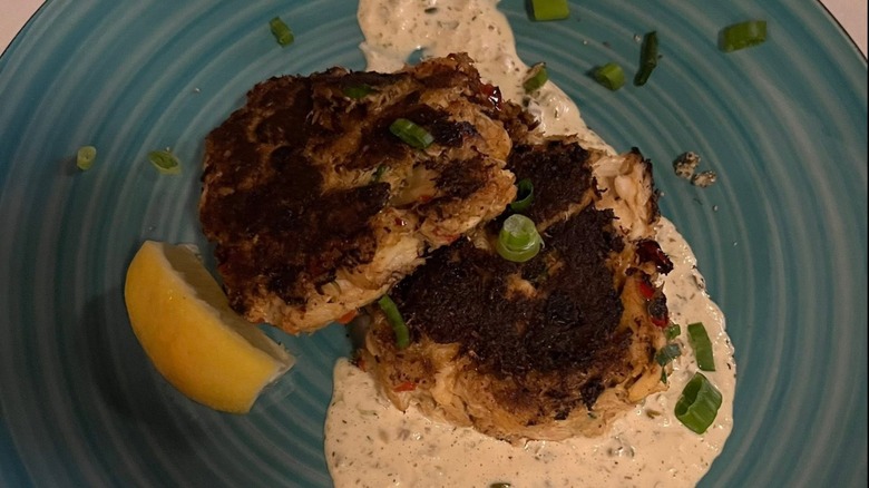 Crab cakes with slice of lemon, remoulade sauce, and sprinkled chives garnish on a blue plate at Grand Central Oyster Bar