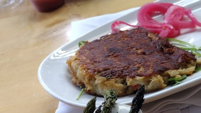 Crab cake with pickled onions on a white platter at Beer & Fish Company