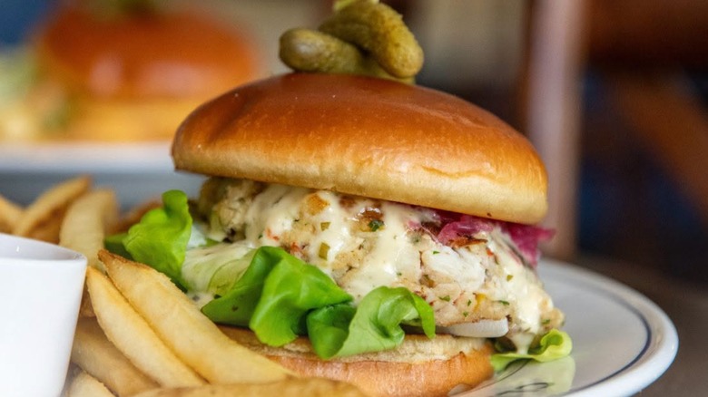 Crab Cake sandwich garnished with gherkins with a side of fries at Claw & Hammer