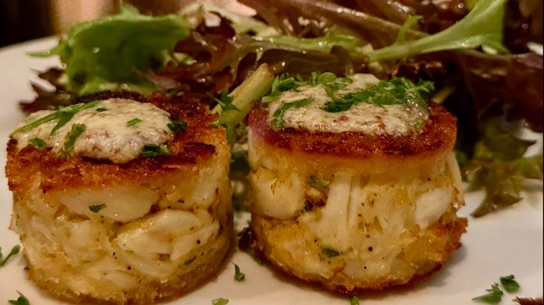 Crab cakes with greens garnished with sauce and herbs at Sperry's