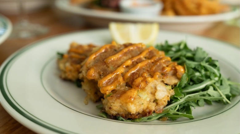 Crab Cake with side of fresh greens on a white plate with a green rim at Market Street Grill