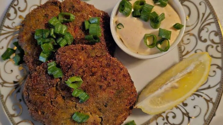 Crab cakes with chive and lemon slice garnish on a white plate with decorative gold pattern at Bourbon Street