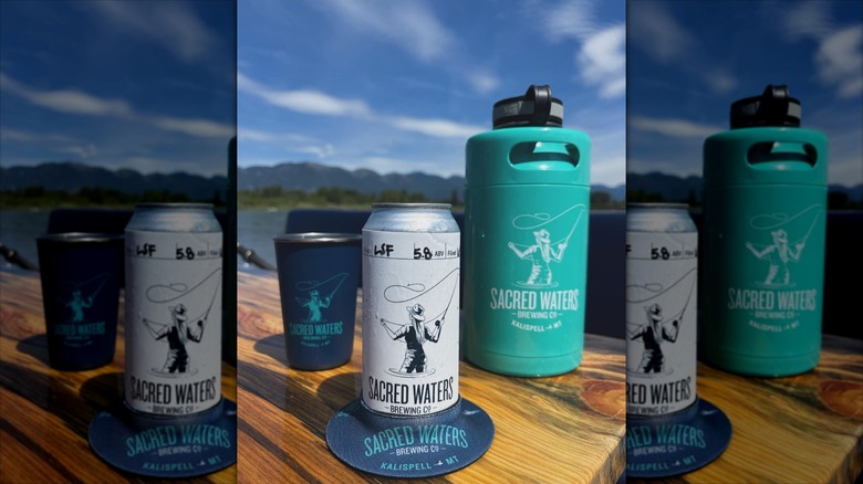 Beer can on coaster with metal cup and water bottle in background on bright day ouside