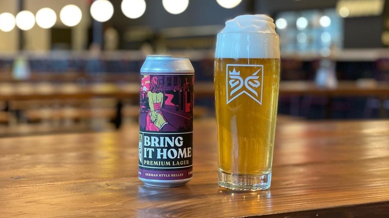 Can of Bring It Home beer on bar counter next to glass of golden beer with lots of foam on top