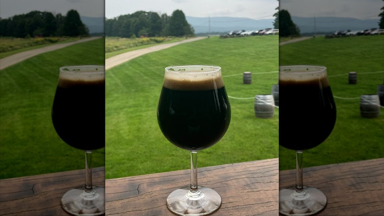 Beer goblet full of dark beer on wooden table outside in front of green lawn