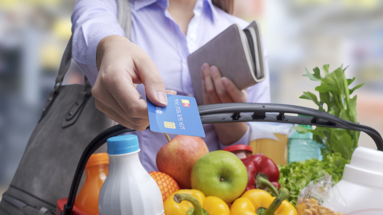 Person handing a blue credit card over a basket full of groceries