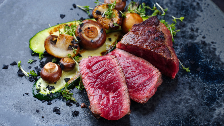 Steak filet cooked rare alongside zucchini and mushrooms