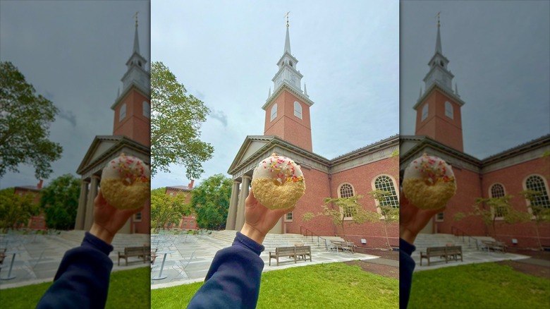 Hand holding donut in front of building at Harvard