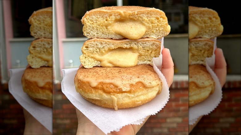 Hand holding three cream-filled donuts on a napkin