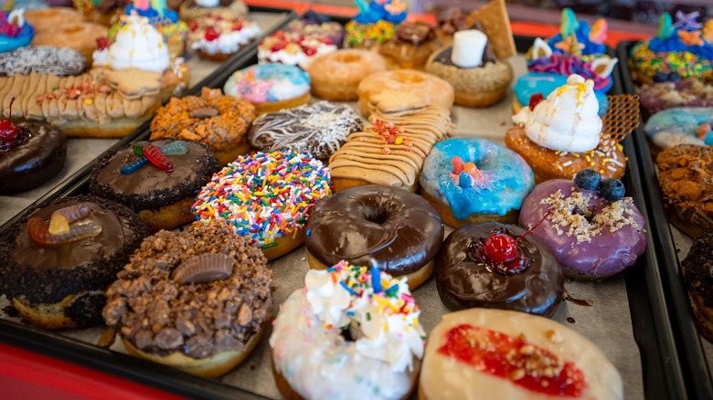 An array of colorful glazed and frosted donuts on a tray