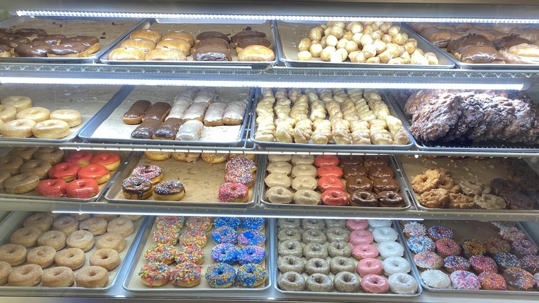 A variety of colorful glazed and iced donuts on trays in glass case