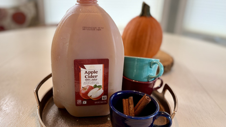 A tray with a jug of Aldi apple cider and cups with cinnamon sticks
