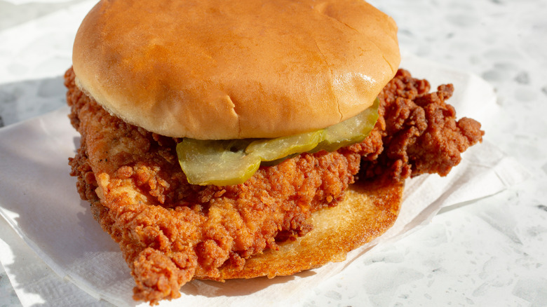 A fried chicken sandwich with pickles on paper napkins