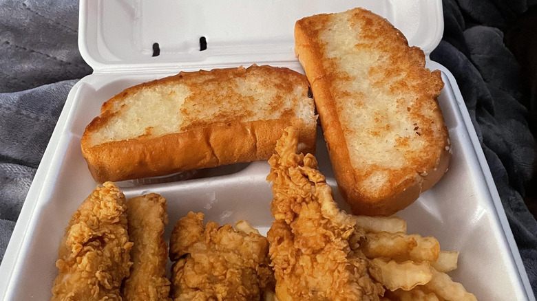 Two pieces of Texas Toast from Raising Cane's sitting above chicken and fries in a styrofoam to-go container