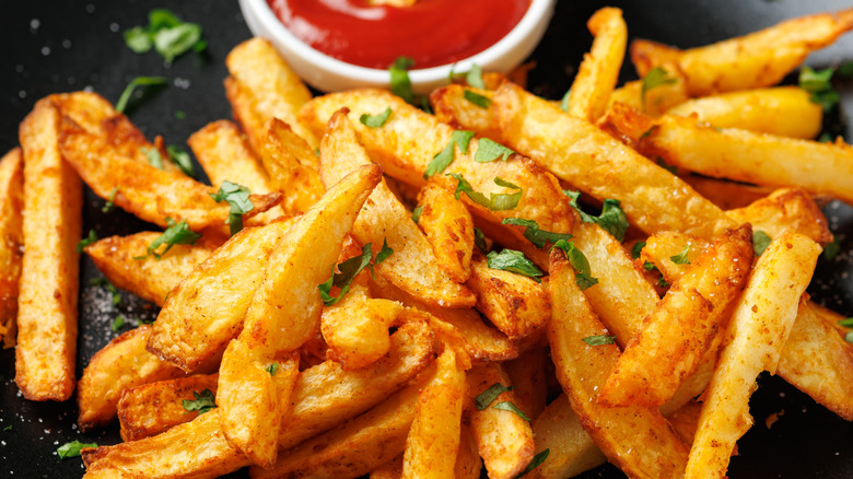 A close up of french fries on a plate with a side of ketchup.