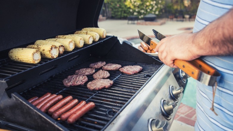 A man grilling hot dogs, hamburgers, and corn on the cob.