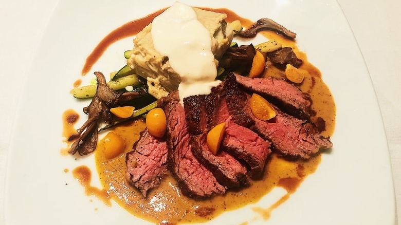 Sliced red meat, veggies, zucchini on white plate