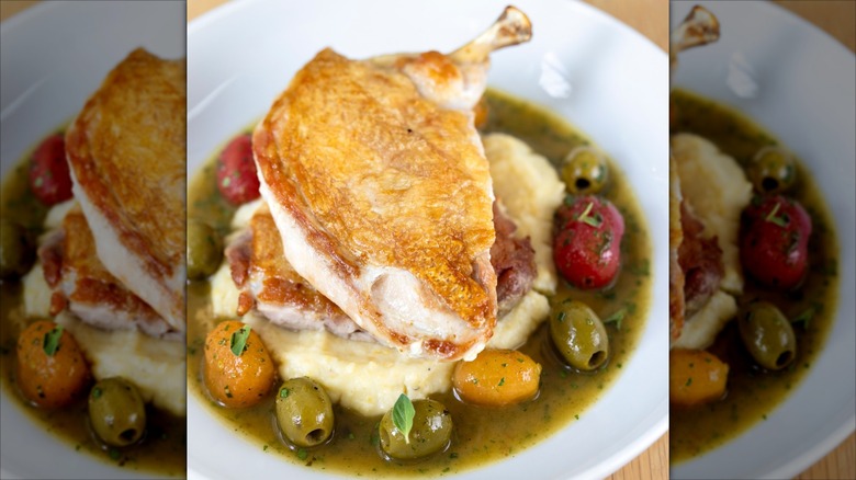 Half chicken on polenta, surrounded by olives on white plates