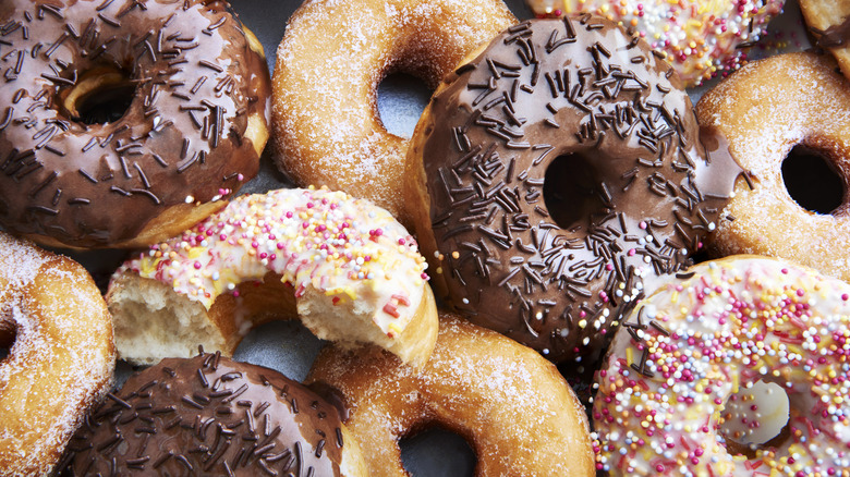 An assortment of different donuts piled on and next to one another.
