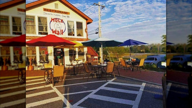 Hole in the Wall exterior with parking lot and tables with umbrellas
