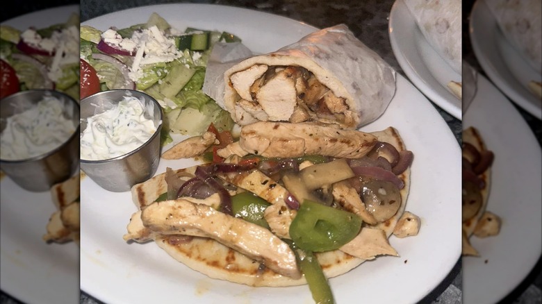 Chicken pita and souvlaki sandwich with tzatziki and a salad on a white plate from Greektown Restaurant