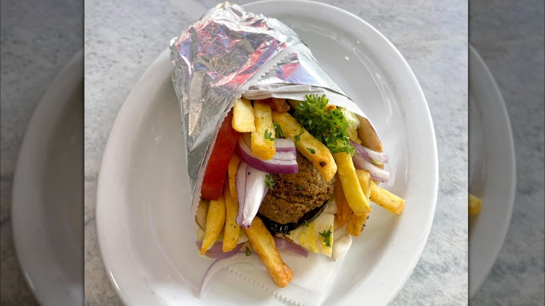 Gyro filled with French fries and falafel, wrapped in foil and placed on a white plate at Katerina's Taverna & Grill