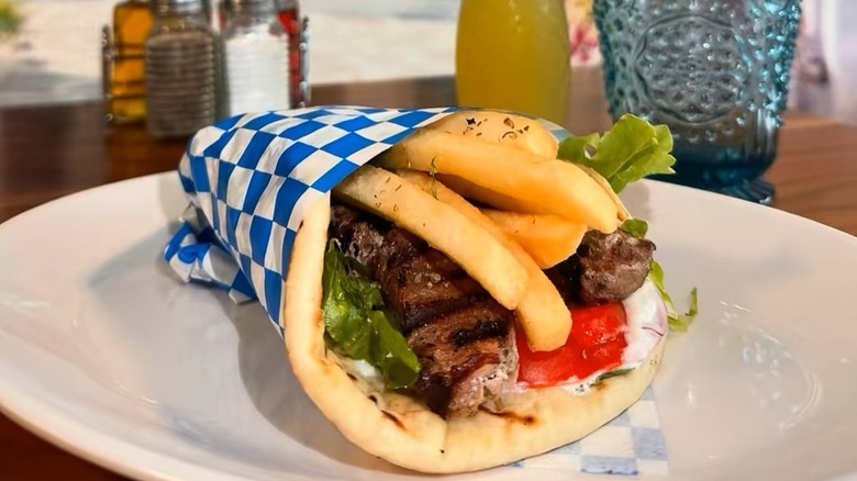 Gyro filled with meat and French fries wrapped in blue and white checkered butcher paper on a white plate at My Big Fat Greek Taverna