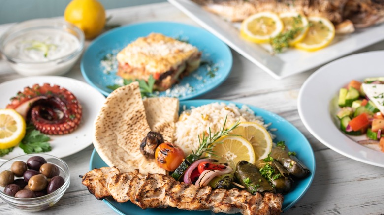 Assorted popular Greek dishes, like souvlaki, moussaka, and stuffed grape leaves, on rustic wooden background