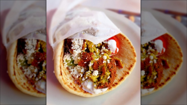 Falafel sandwich wrapped in butcher paper from Olympic Flame Restaurant on a white plate