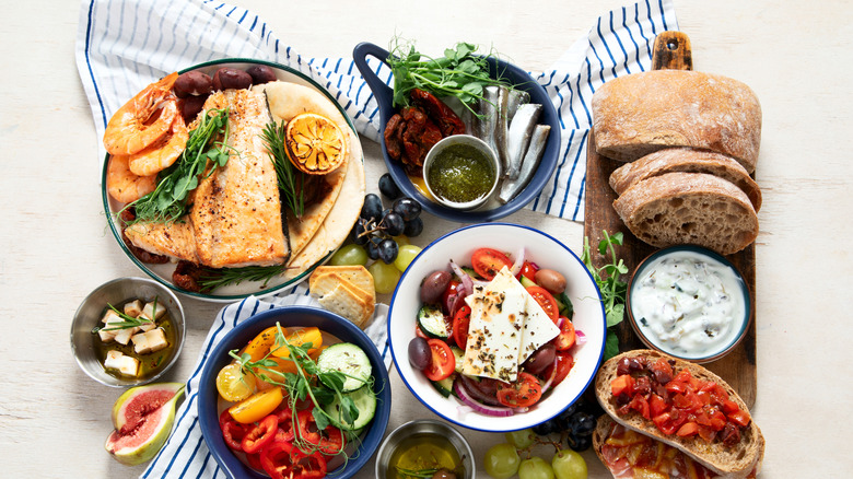 Greek food background of fish, pita, greek salad, tzatziki, feta, olives, bread, and more