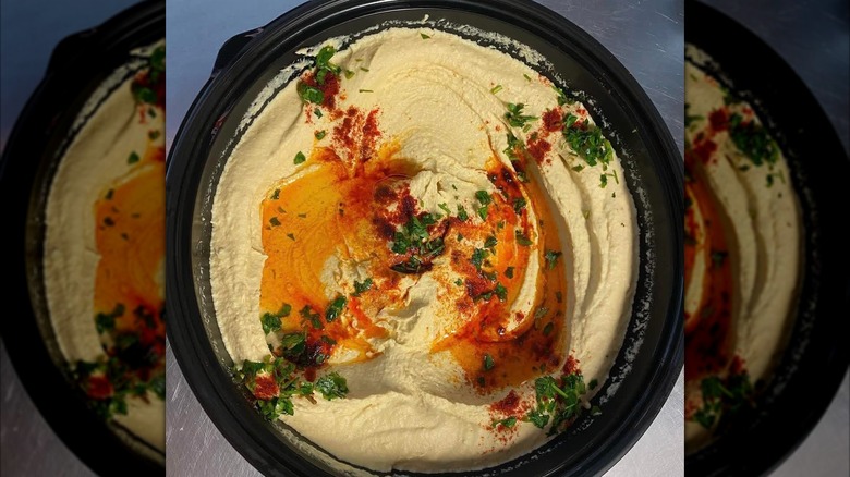 Hummus from Trieste Cafe on a black plate garnished with olive oil, paprika, and fresh herbs
