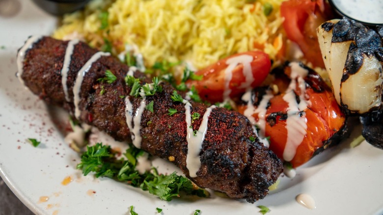 Kebab with sauce, rice, and grilled vegetables on a white plate from Petra Cafe Greek & Mediterranean