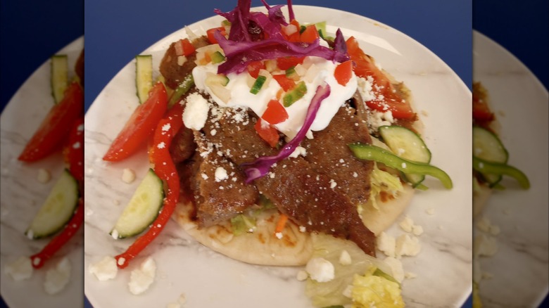 Greek meat dish on pita with vegetables and feta on a white plate from El Greco