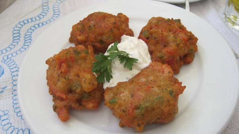 Tomato Keftedes on a white plate garnished with tzatziki and fresh parsley from Jim & Jennie's Greek Village