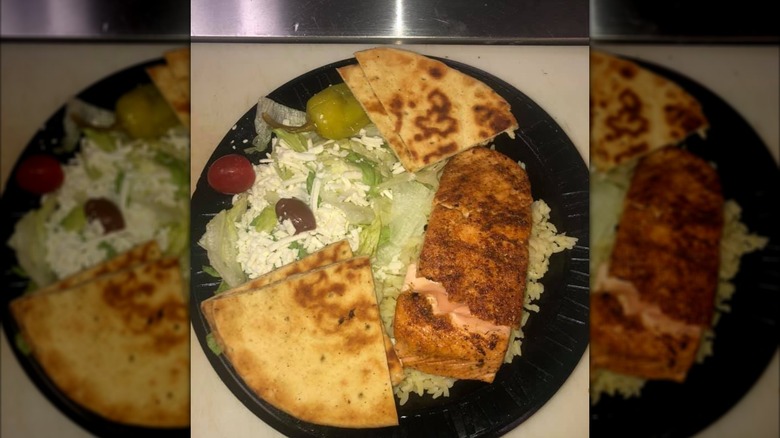 Greek salad, pita, and meat on a black plate from Greek Boys